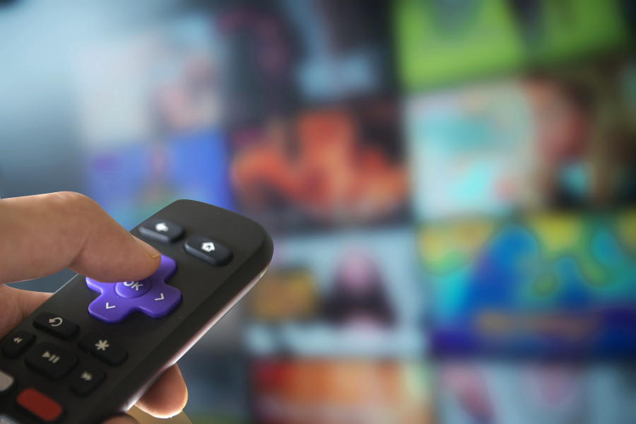 Mano toma control remoto; fuera de foco, pantalla de TV