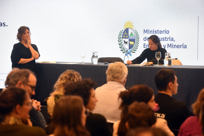 Al fondo, Cardona anota, en la misma mesa que Schroeder; más cerca, público; detrás, pantalla